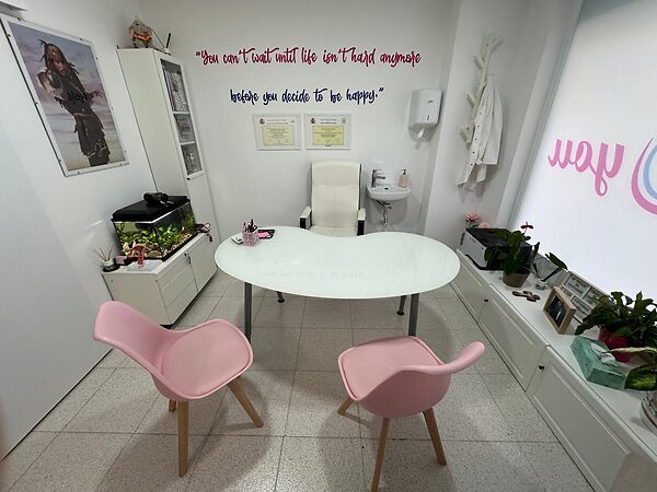 Sala de consulta de la Dra. Helena Marcos con sillas rosas, mesa redonda, plantas y frase motivacional